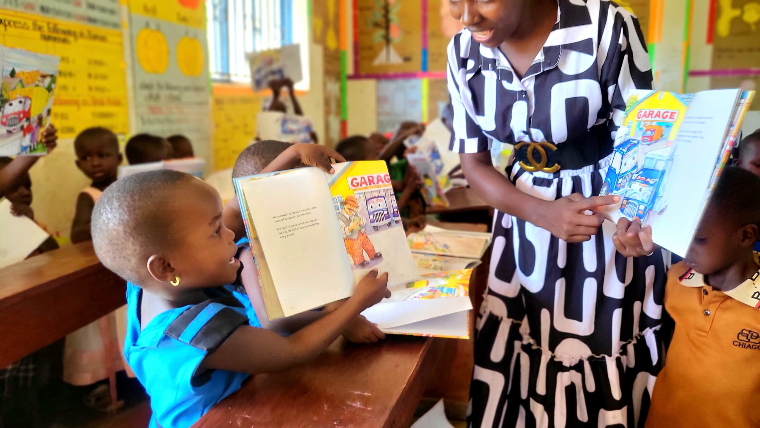Teacher leans warmly toward a young learner sharing a book at their desk