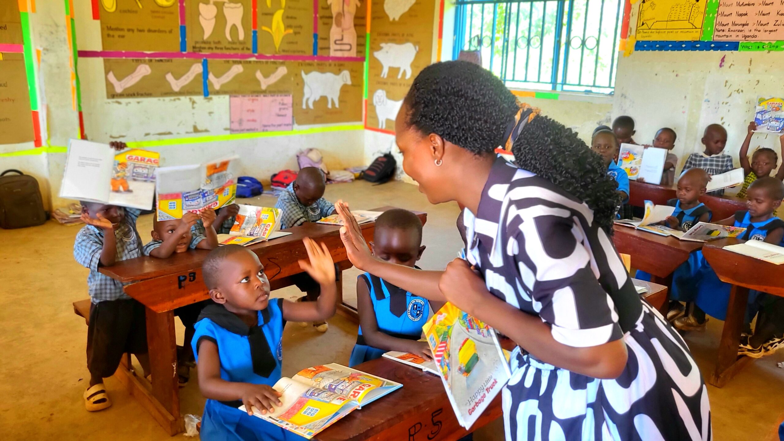 Teacher offers a high-five to a young boy amid a room full of reading students