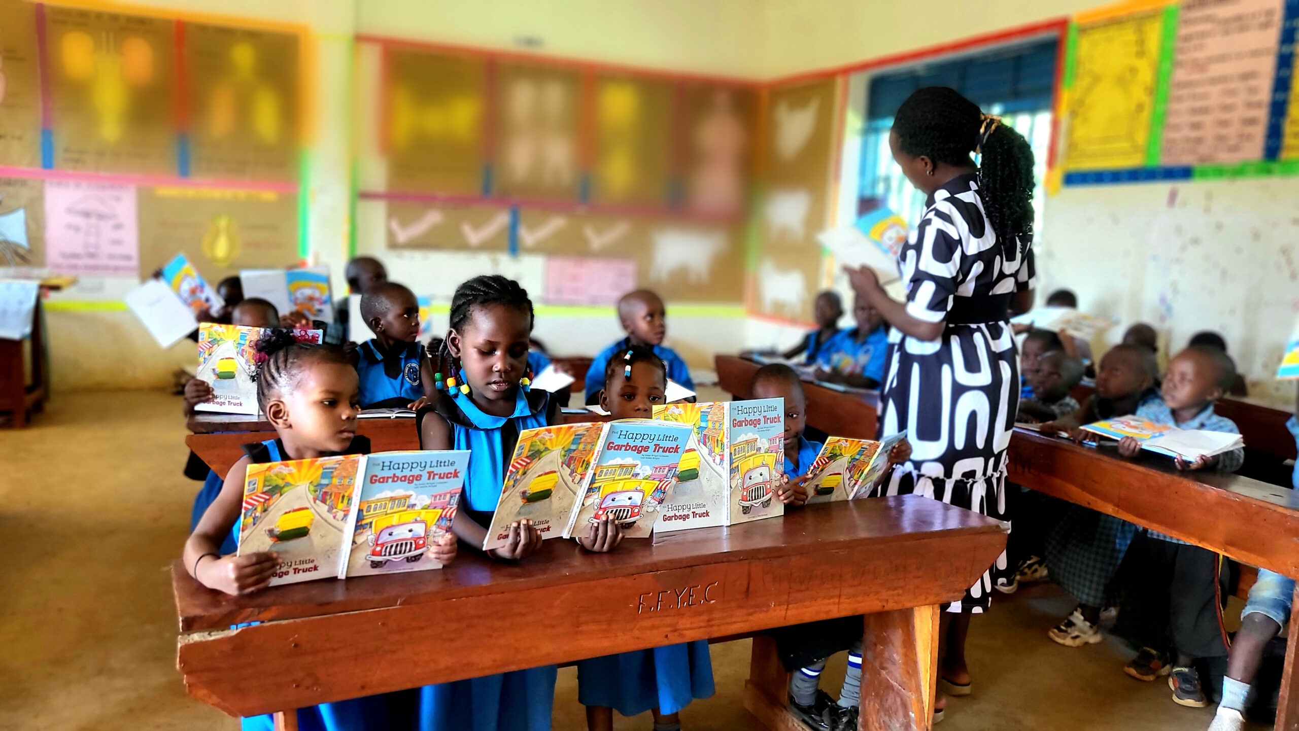 Students hold up their Happy Little Garbage Truck books with excitement — F.F.Y.E.C. engraved on their desks